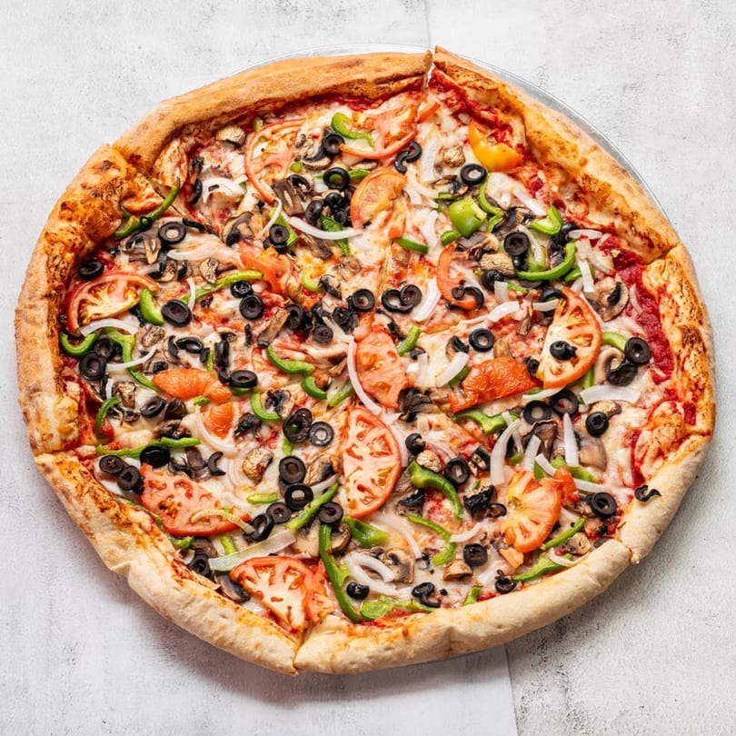 A whole vegetarian pizza, topped with tomatoes, onions, green peppers, mushrooms, and black olives.