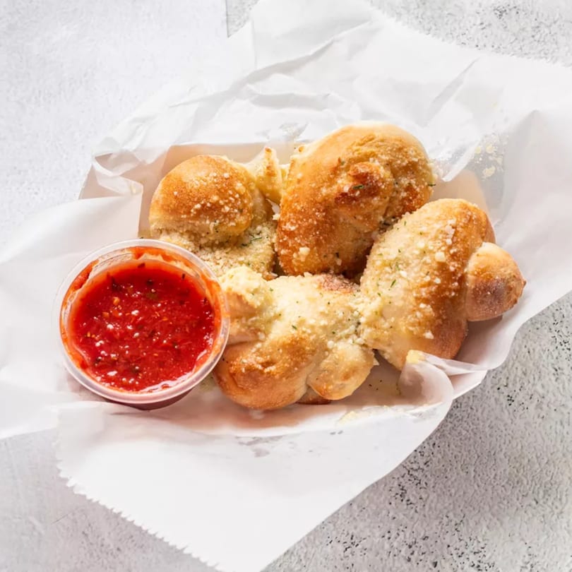 Garlic knots dusted with Parmesan cheese and herbs, served with a side of marinara sauce.