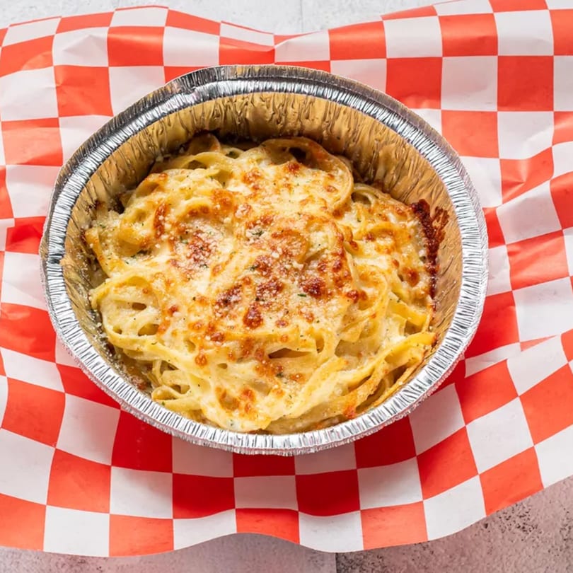 Baked pasta with melted cheese in a foil container on red and white checkered paper.