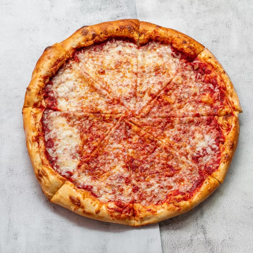 A whole cheese pizza, cut into eight slices, on a light gray surface.