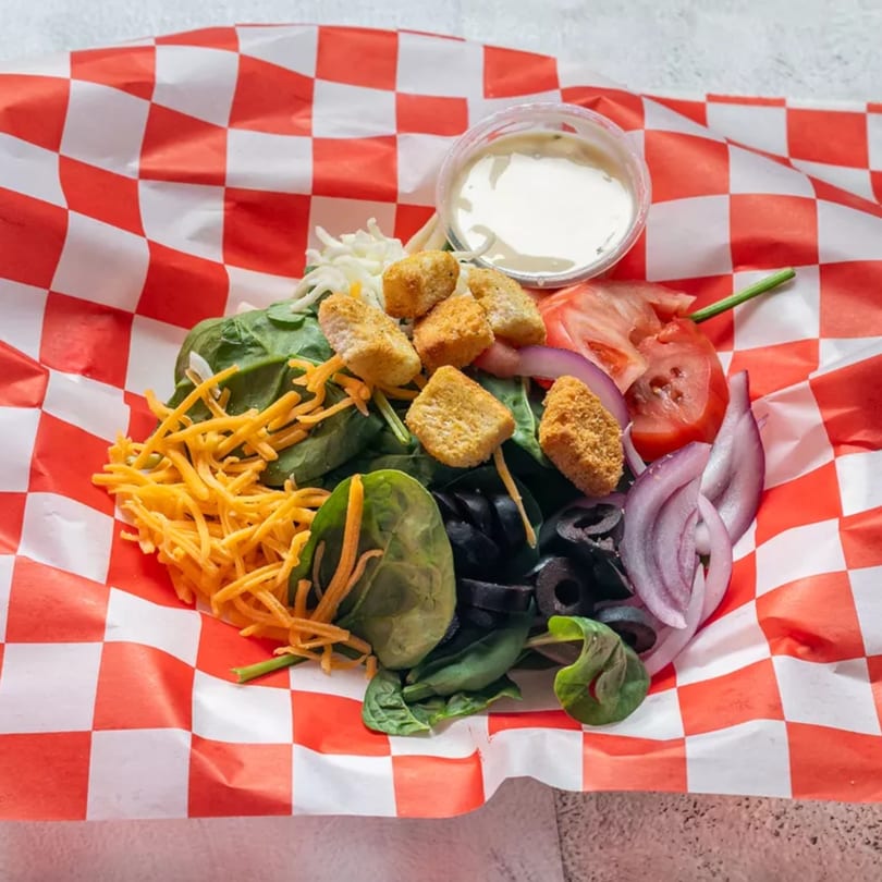 Fresh salad with spinach, cheese, croutons, tomatoes, olives, and red onion, with dressing on the side.